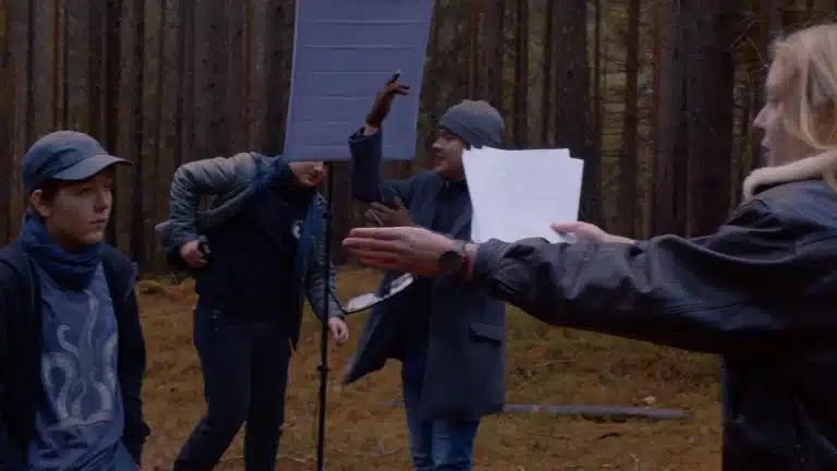 Ein Regisseur und Schauspieler streiten sich im Vordergrund, der Schauspieler mit Drehbuch in der Hand. Im Hintergrund holt eine Person ein Messer heraus, während eine andere sich gerade aufregt.