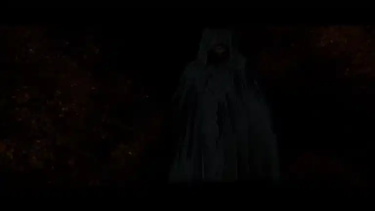 Eine dunkle Gestalt in Umhang steht vor einem dunklen Hintergrund.