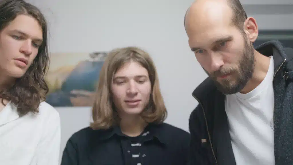 Drei Männer stehen in einem hellen weißen Raum um etwas herum.