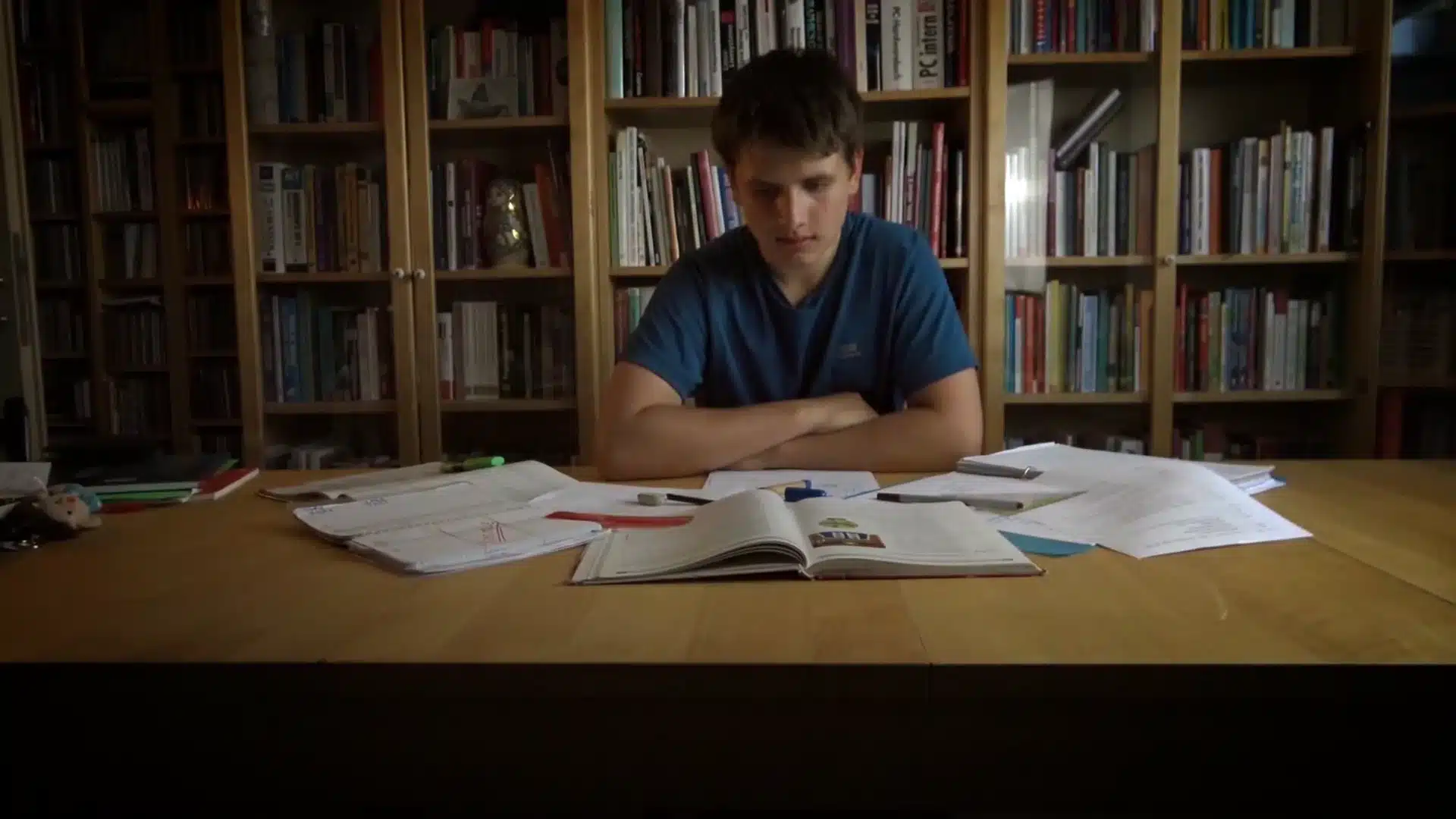 Ein Junge sitzt vor einem Bücherregal und hat viele Zettel um sich herum liegen.